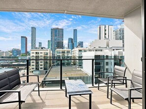 Ein Balkon mit Sitzgelegenheit, einem Tisch und Blick auf die Stadt.