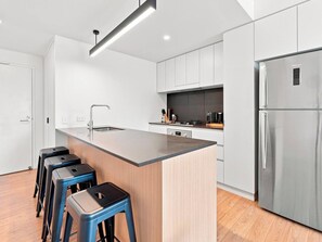 Une cuisine moderne dotée d’un îlot central, de tabourets de bar, d’appareils électroménagers en acier inoxydable et de meubles de couleur claire.