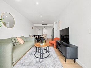 Un salon moderne comprenant un canapé, une table basse ronde, un meuble pour la télévision et un coin repas avec des chaises et une table.