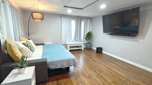 Un dormitorio moderno con cama, mesita de noche, lámpara y televisor montado en la pared.