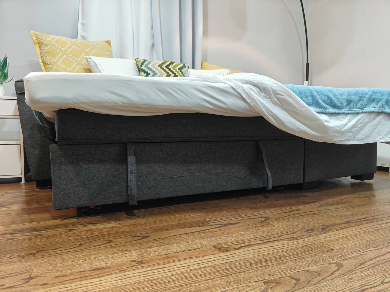 Una cama con cabecera tapizada en gris, ropa de cama blanca y una manta azul.