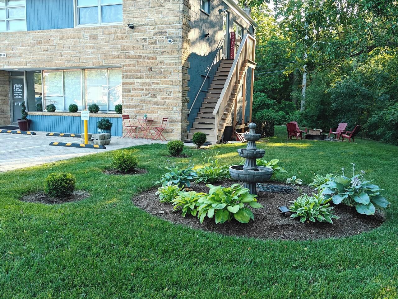 A building with a stone facade, a staircase, and a garden with a fountain.