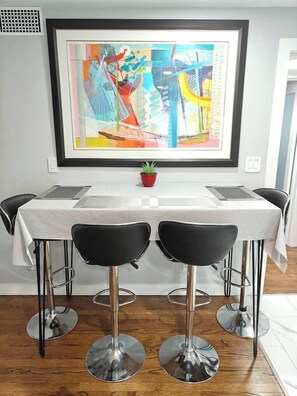 Espaço de refeições com mesa branca, cadeiras pretas e um quadro abstrato colorido acima.