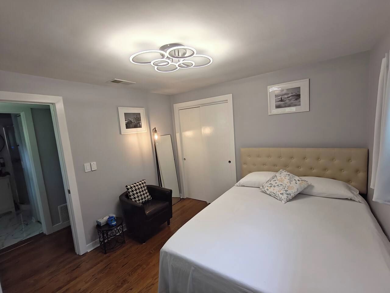 A bedroom with a bed, a chair, a door, and a ceiling light fixture.