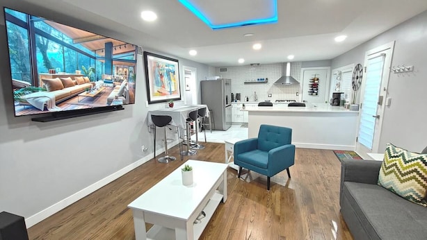 Una sala moderna con un televisor de pantalla plana, una mesa de centro, un sillón azul y un sofá gris.