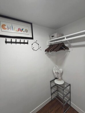 A corner of a room with a white wall, a framed picture, a white fan, and a metal rack.