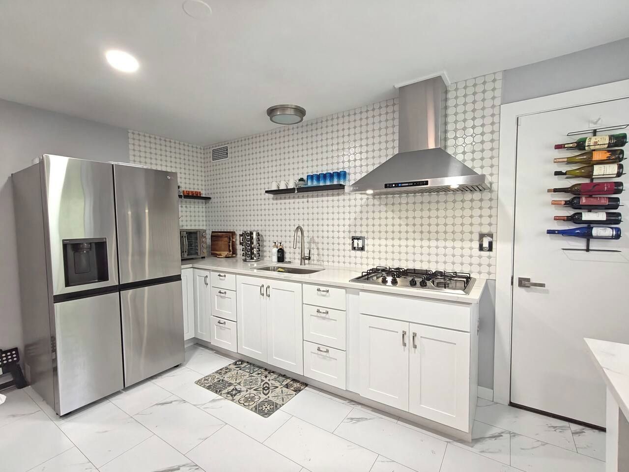 Una cocina moderna con un refrigerador de acero inoxidable, armarios blancos, una estufa a gas y una estantería para vinos.