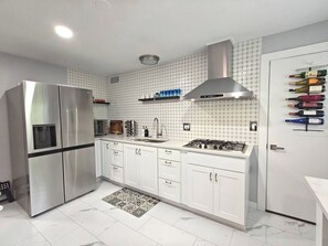 A modern kitchen with a stainless steel refrigerator, white cabinets, a gas stove, and a wine rack.