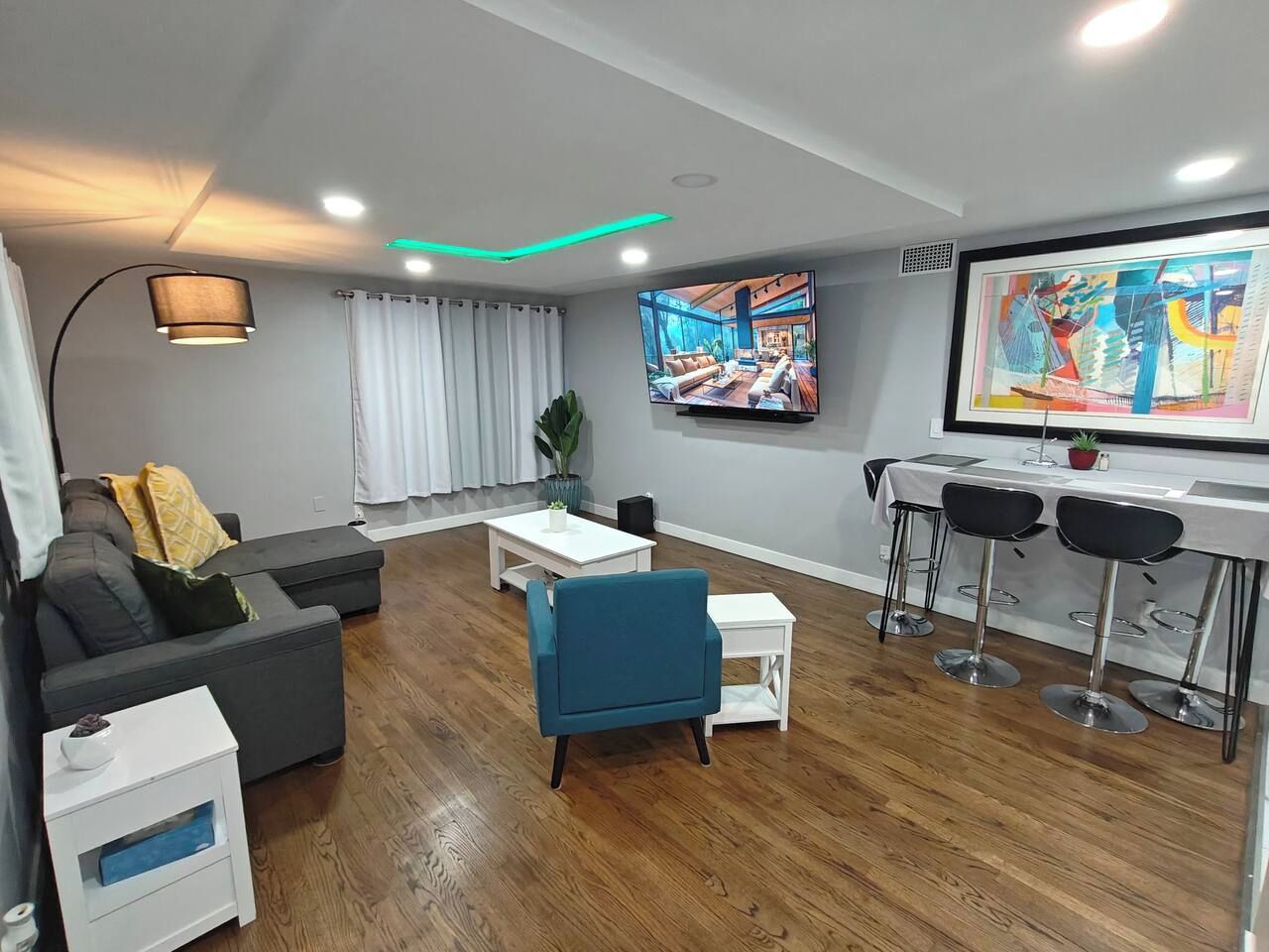 Una sala de estar moderna con un sofá, un sillón azul, una mesa de centro y un televisor montado en la pared.
