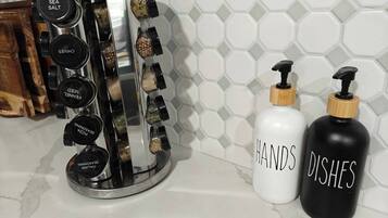 A kitchen counter with a spice rack, two labeled bottles, and a hexagonal tiled backsplash.