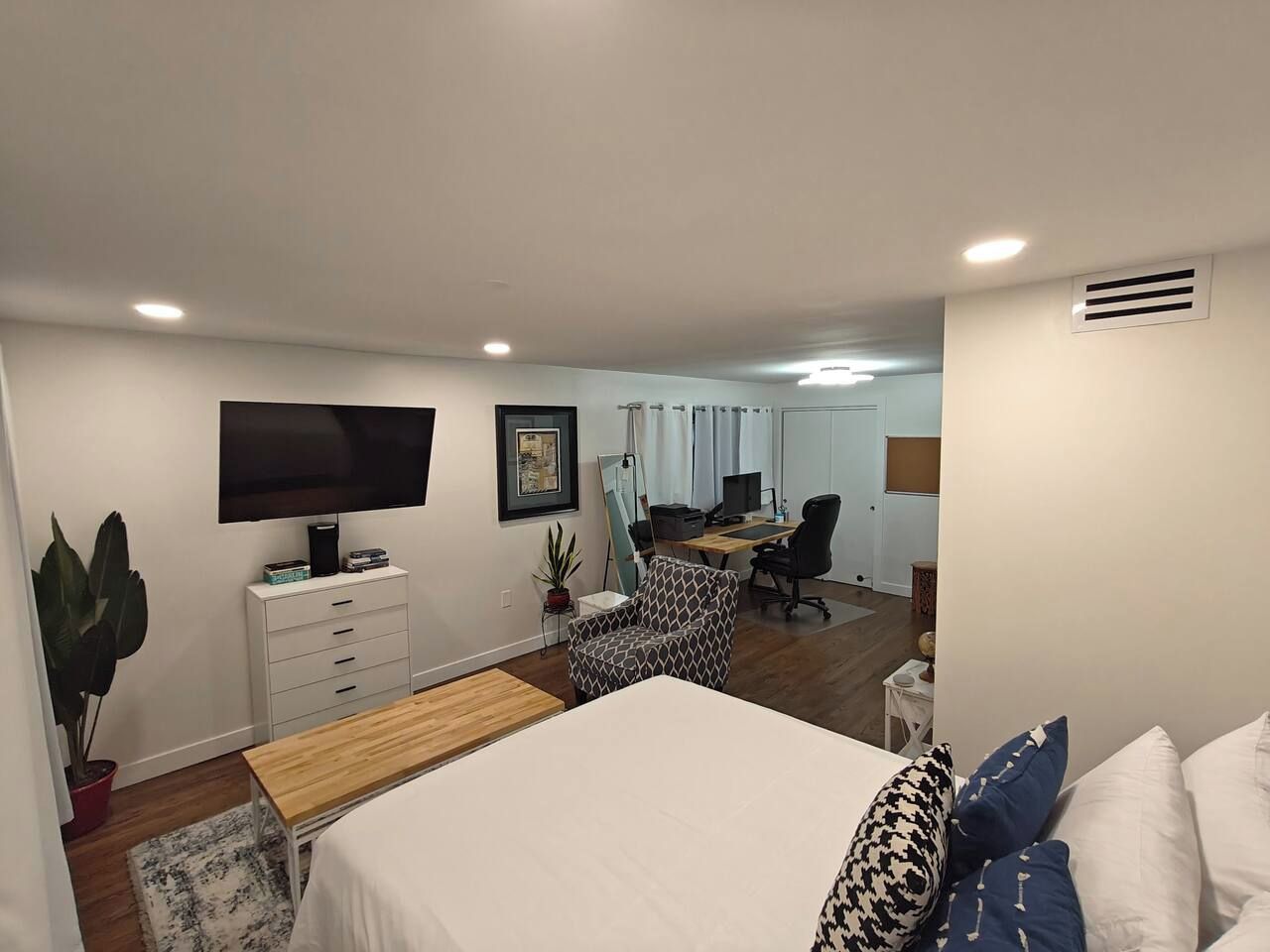 A bedroom with a bed, a desk, a chair, a television, and a potted plant.