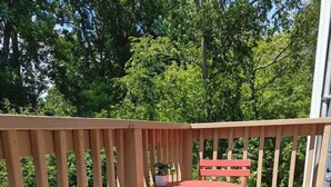 Una terraza de madera con una mesa y sillas de metal rojo, rodeada por un barandal de madera.