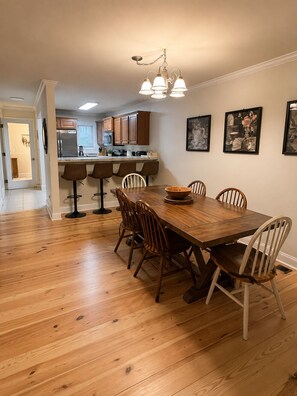 Un comedor con mesa y sillas de madera, una cocina al fondo y obras de arte en la pared.