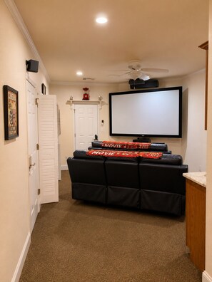 Ein Heimkino mit großem Flachbildfernseher, schwarzen Ledersesseln und Deckenventilator.