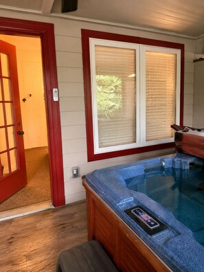 Un bain à remous doté d’un panneau de commande, d’un banc en bois et d’une porte donnant sur un espace extérieur.
