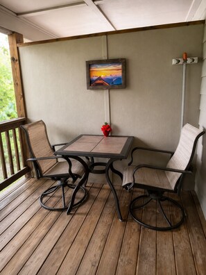 Eine Holzterrasse mit Tisch und Stühlen, einem Bild an der Wand und einer roten Blumenvase.