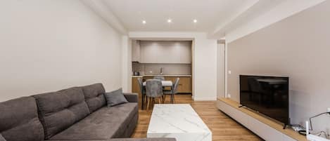 Un salon moderne avec un canapé gris, une table basse blanche et un téléviseur à écran plat posé sur une étagère en bois.