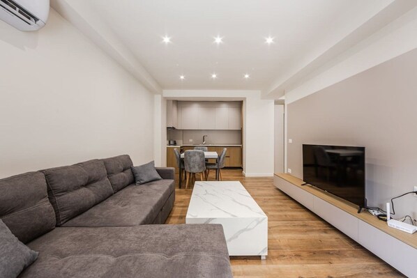 Ein modernes Wohnzimmer mit einem grauen Sofa, einem weißen Couchtisch und einem Flachbildfernseher auf einem Holzregal.