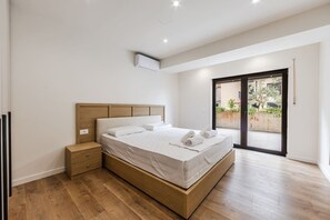 Quarto moderno com cama de madeira, mesa de cabeceira e porta de vidro deslizante para área externa.