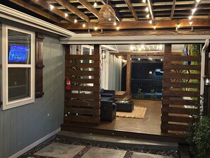 A covered outdoor area with a wooden deck, seating, and a view of the backyard. - Charming Country Home! (Azle)