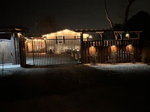 A gated property at night with a well-lit entrance and a covered porch area. - Charming Country Home! (Azle)