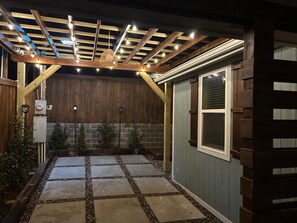 A covered patio area with a stone pathway, wooden beams, and a brick wall. - Charming Country Home! (Azle)