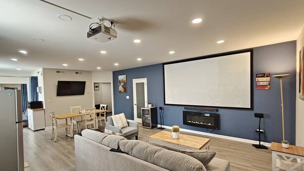 A modern living room with a sofa, coffee table, and a fireplace. There is a dining area with a table and chairs, and a kitchen area with a refrigerator. - The Modern Loft & Patio (Waukegan)