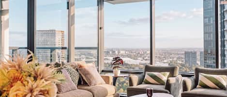 A modern lounge with a sofa, armchairs, and a coffee table, featuring a city view through large windows.