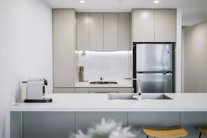A modern kitchen with a stainless steel refrigerator, a gas stove, and a white countertop. - The Sky Perch 2- Walking distance to Accor stadium and Qudos bank arena (Sydney Olympic Park)