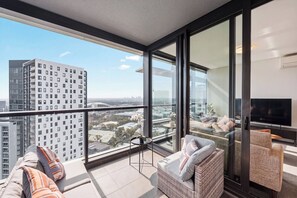 A modern apartment with a balcony, large windows, and a flat-screen TV. - The Sky Perch 2- Walking distance to Accor stadium and Qudos bank arena (Sydney Olympic Park)