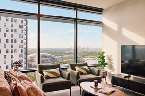 A modern living room with a large window, a sofa, two armchairs, a coffee table, a TV, and a plant.