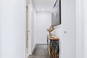 A hallway with a wooden console table, a potted plant, and a framed artwork on the wall. - The Sky Perch 2- Walking distance to Accor stadium and Qudos bank arena (Sydney Olympic Park)