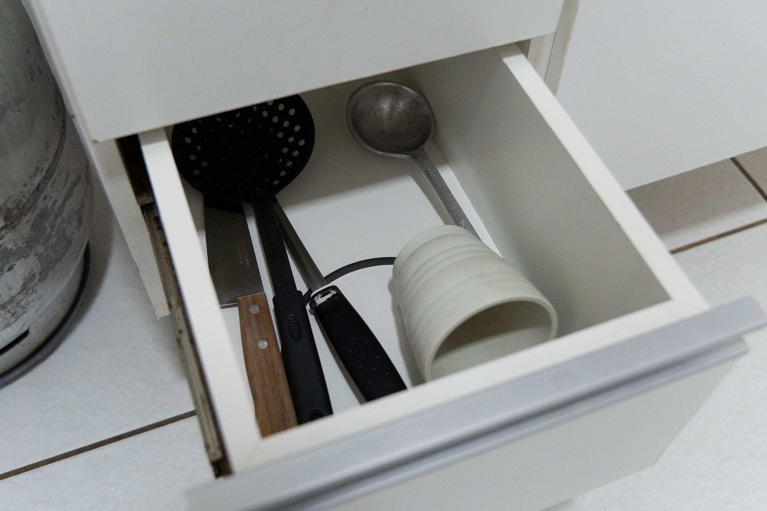 A drawer with kitchen utensils including a spatula, a rolling pin, and a measuring cup.