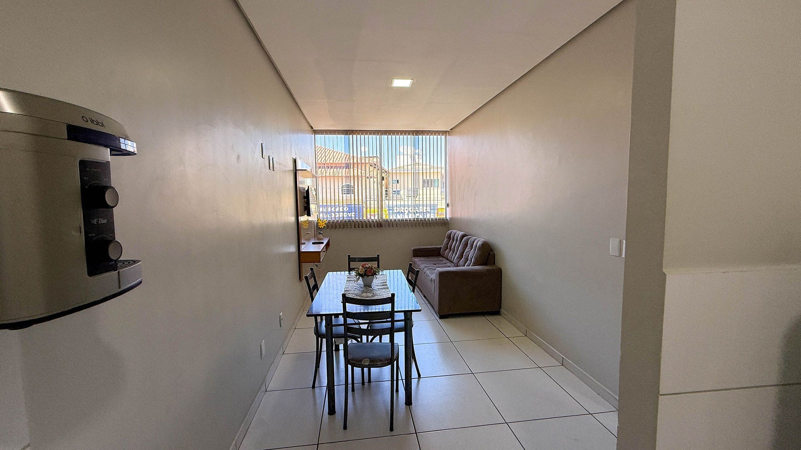 A compact living space with a dining area, a sofa, and a small kitchen area with a refrigerator and a microwave.