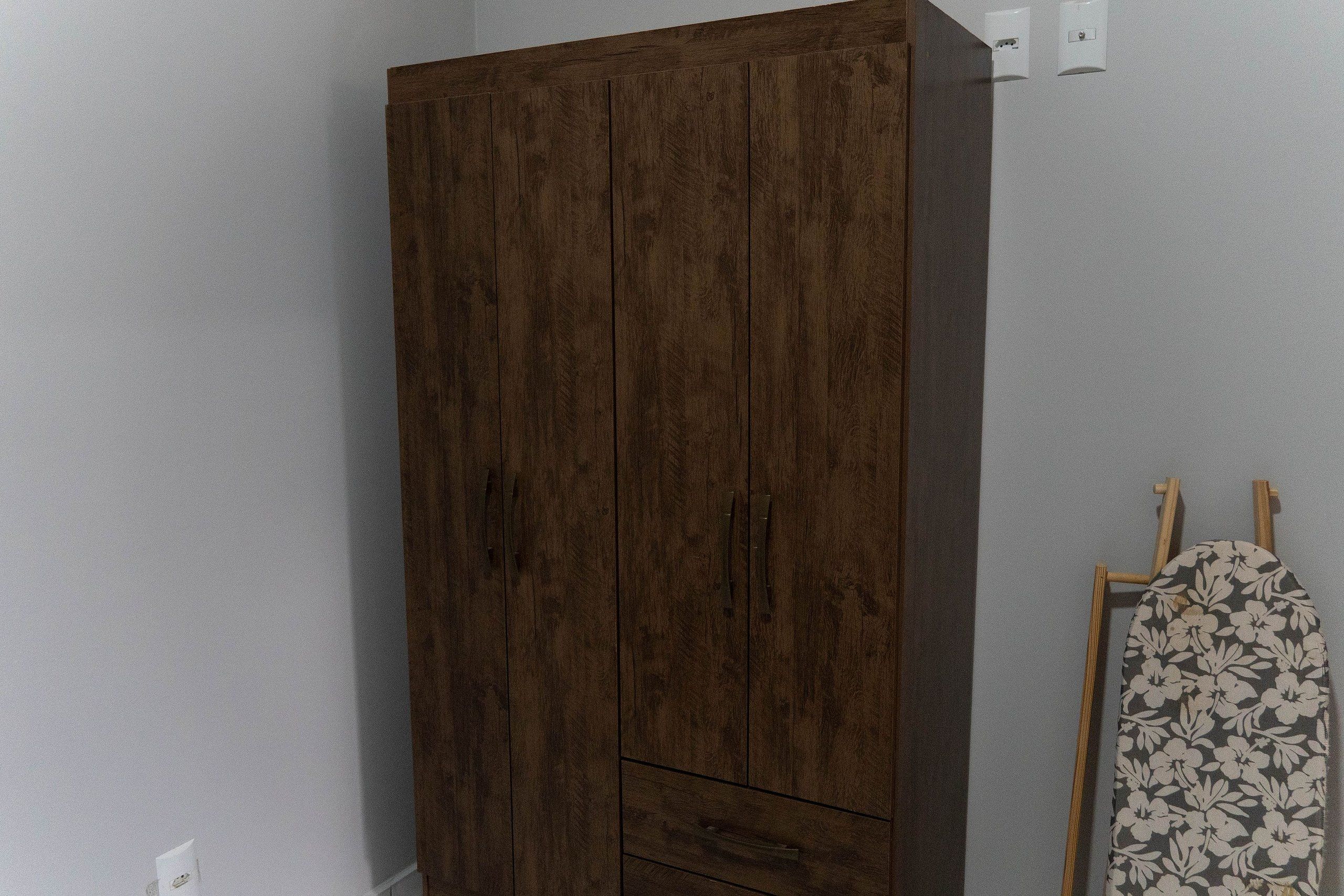 A wardrobe with a dark wood finish, a small drawer, and a hanging rod with a floral pattern.