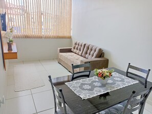 A dining area with a table, chairs, a sofa, and a window with blinds. - CONDOMINIO SONHARE - 101 (ANAPOLIS)