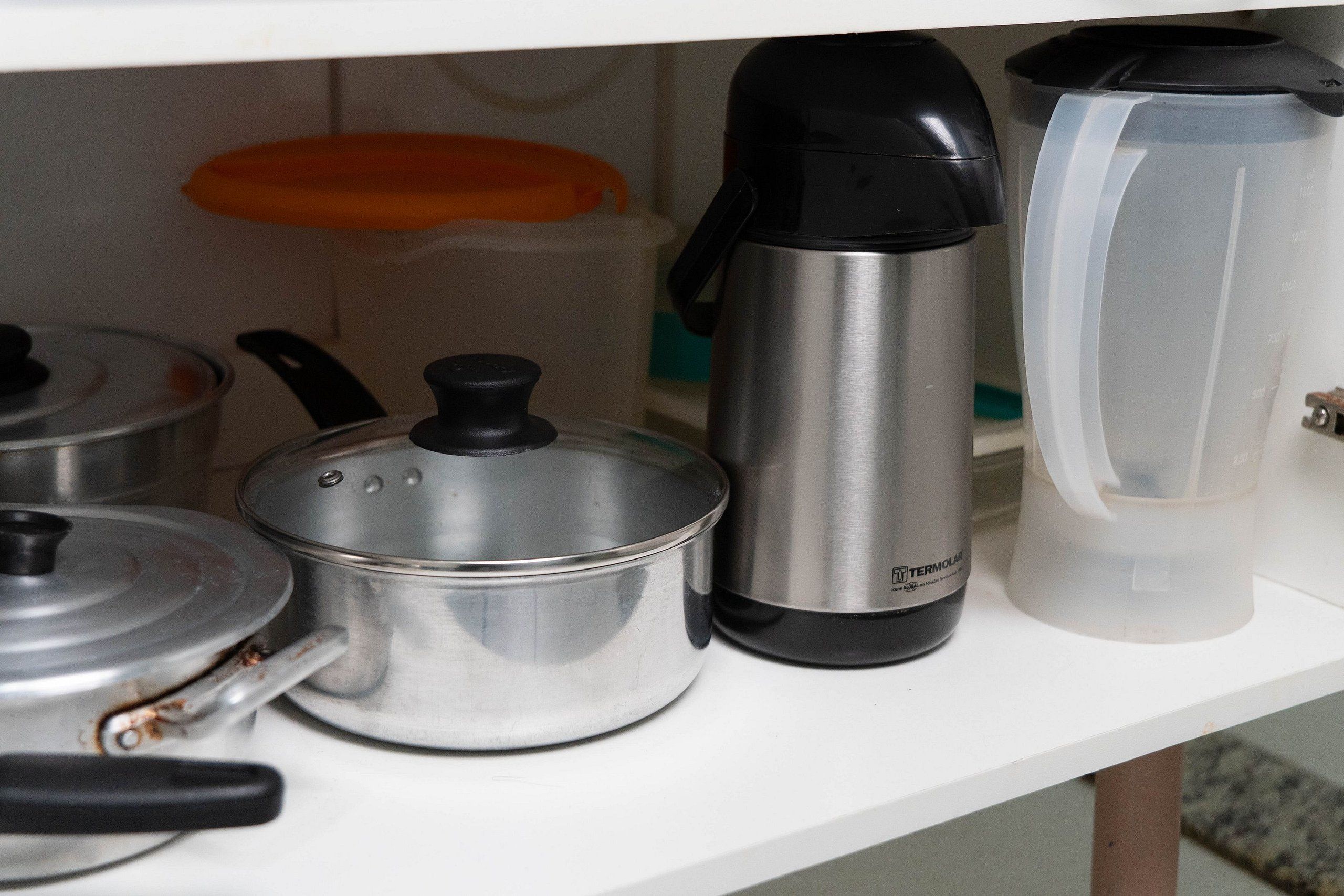Uno scaffale in cucina con pentole in acciaio inox, un bollitore elettrico nero e una thermos trasparente.