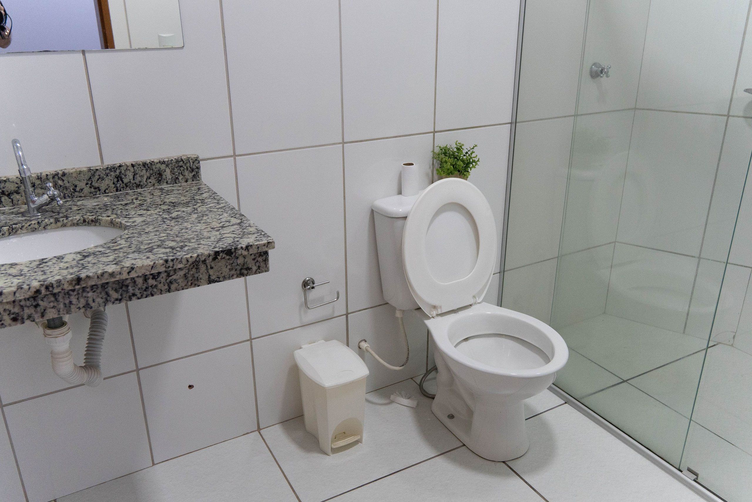 A bathroom with a granite countertop, a toilet, a small trash bin, and a glass shower enclosure.