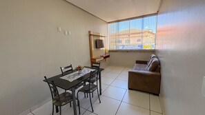 Una habitación pequeña y luminosa con una mesa de comedor, sillas, un sofá y un televisor montado en la pared.