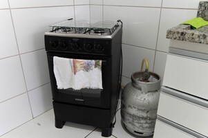 Cozinha compacta com fogão preto, cilindro de gás e painel de azulejos.