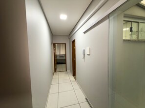 Un pasillo estrecho con suelo de baldosas, una puerta al final y un teléfono sujeto a la pared.