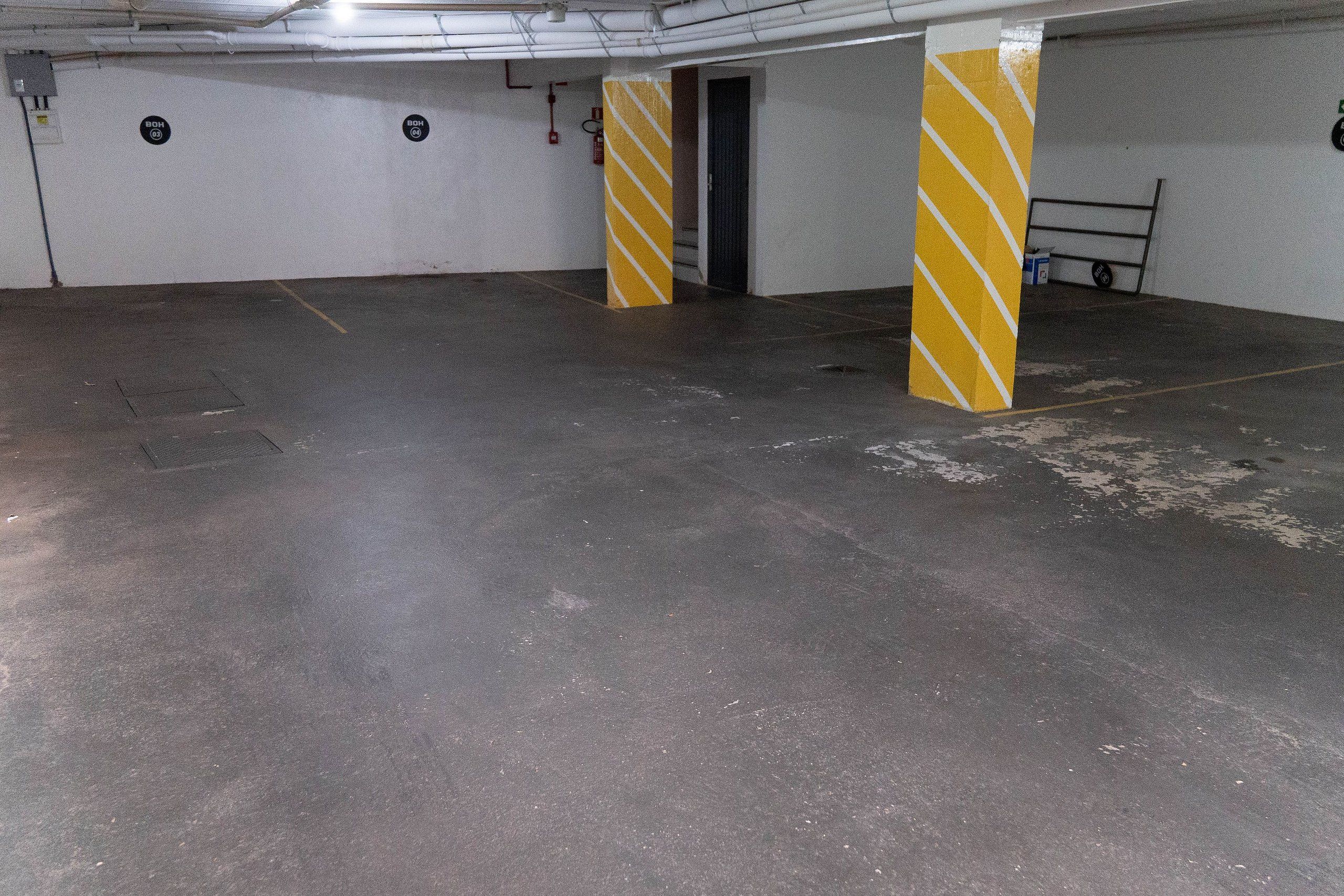Maanalainen pysäköintialue, jossa on betonilattia ja keltaisilla raidoilla varustetut pilarit.