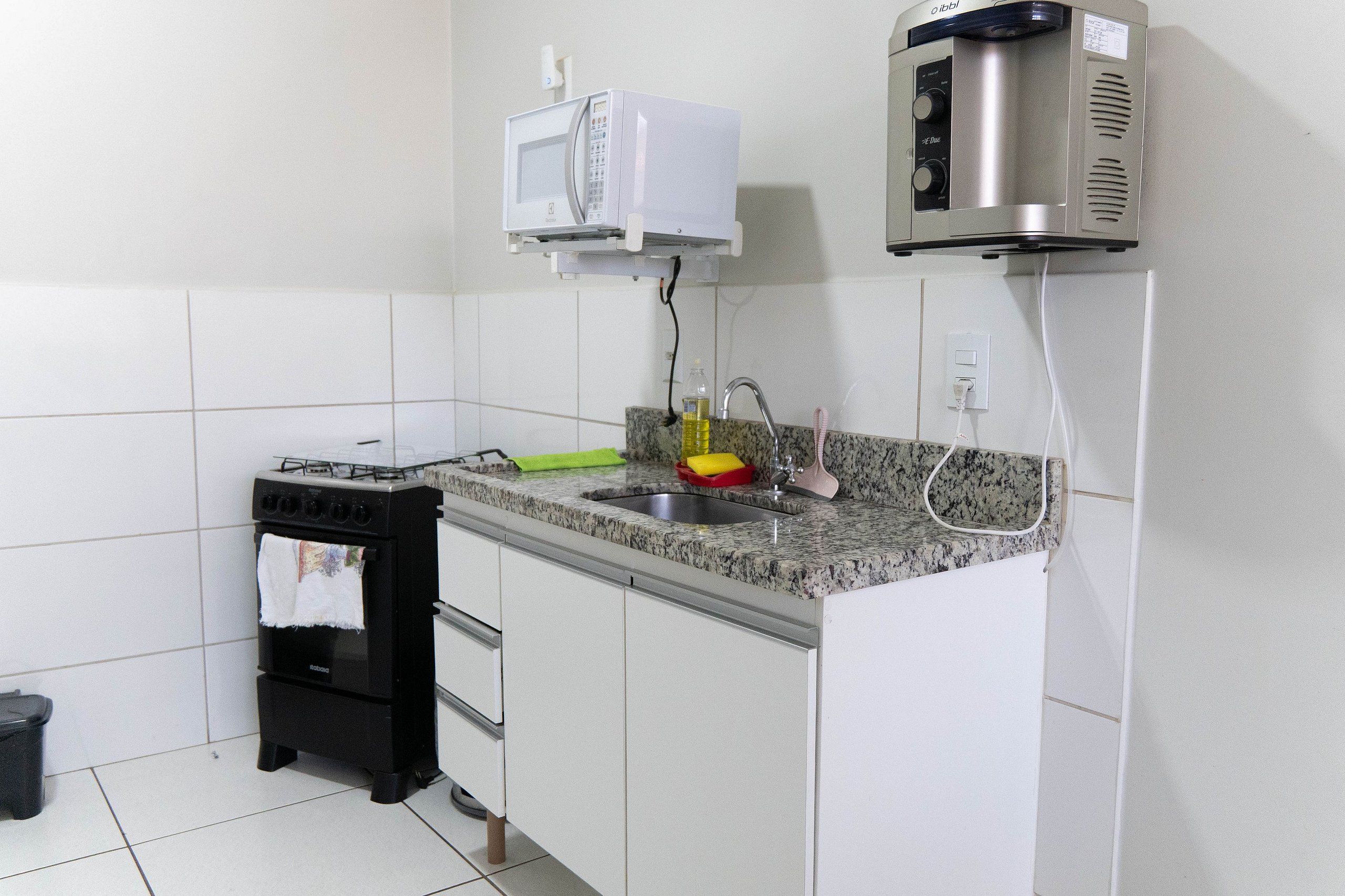 Una cocina compacta con microondas integrado, cafetera, pileta y horno pequeño.