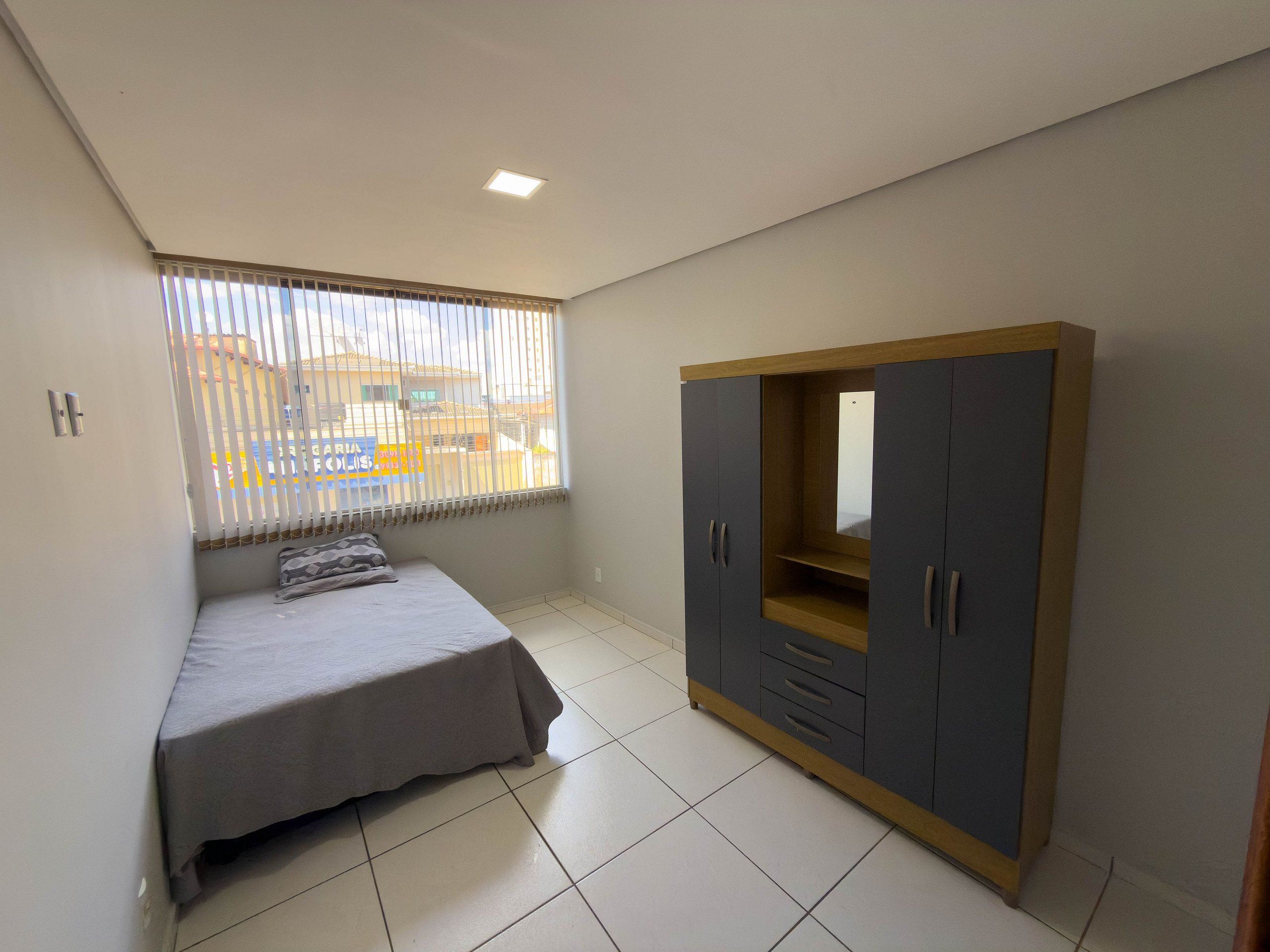 A bedroom with a bed, a wardrobe, and a window with blinds.
