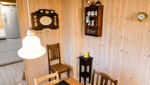 Een kamer met houten lambrisering, een eettafel, stoelen, een klok en een kast met servies.