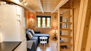 Een compacte kamer met een kitchenette, een bank, een klein tafeltje en een houten plankunit.