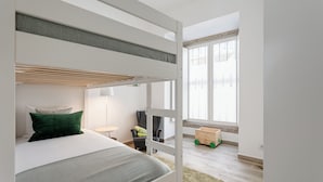 Ein Stockbett mit Schreibtisch und Stuhl, ein Fenster mit Vorhängen und ein kleines Holzautos Spielzeug.