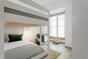 A bunk bed with a desk and chair, a window with curtains, and a small wooden toy car. - Baixa Garden: 2BR + Patio | Perfect for Families (Lisboa)