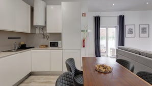 Eine moderne Küche mit weißen Schränken, einer Mikrowelle und einem Durchlauferhitzer. Es gibt einen Essbereich mit einem Holztisch und gepolsterten Stühlen.
