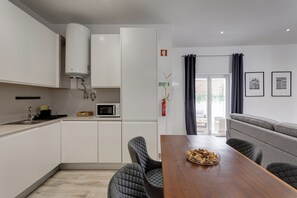A modern kitchen with white cabinets, a microwave, and a water heater. There is a dining area with a wooden table and cushioned chairs. - Baixa Garden: 2BR + Patio | Perfect for Families (Lisboa)
